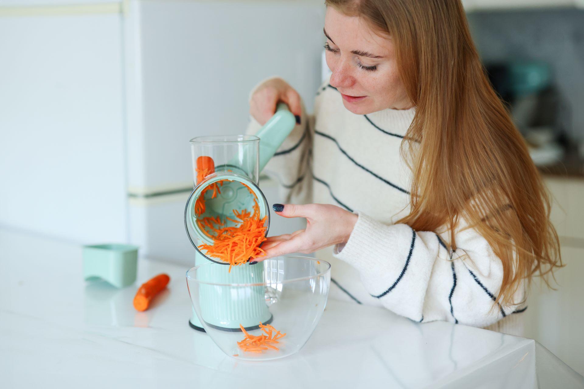 Frau nutzt elektrischen Gemüseschneider zum Raspeln von Karotten