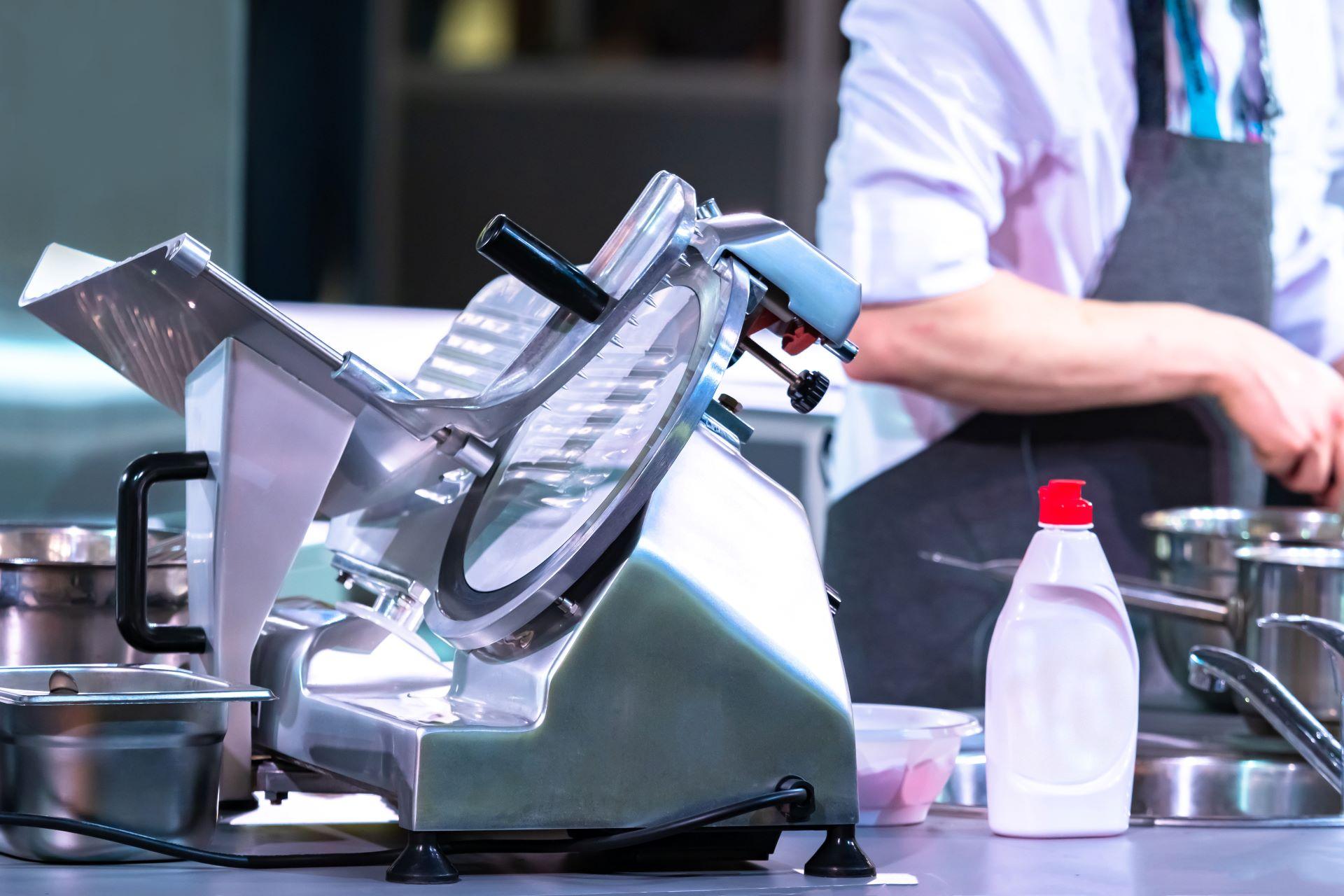 Elektrischer Gemüseschneider aus Edelstahl auf Arbeitstisch mit Reinigungsmittel